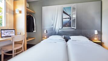 A hotel room with a bed, a desk with a computer, a chair, and a wardrobe.