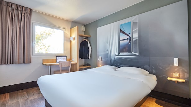 Una habitación de hotel con una cama grande, un escritorio con computadora, una silla y un armario.