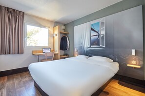 Una habitación de hotel con una cama grande, un escritorio con computadora, una silla y un armario.