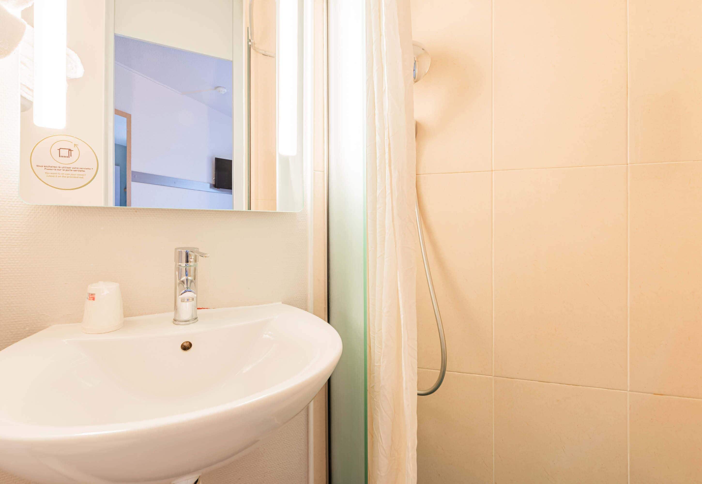 Un bagno con lavandino bianco, uno specchio e una tenda da doccia.