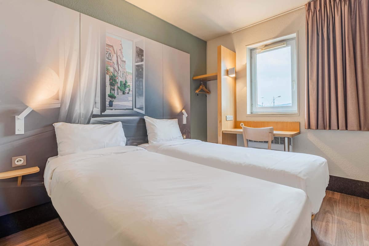 Een hotelkamer met twee bedden, een bureau en een raam met gordijnen.
