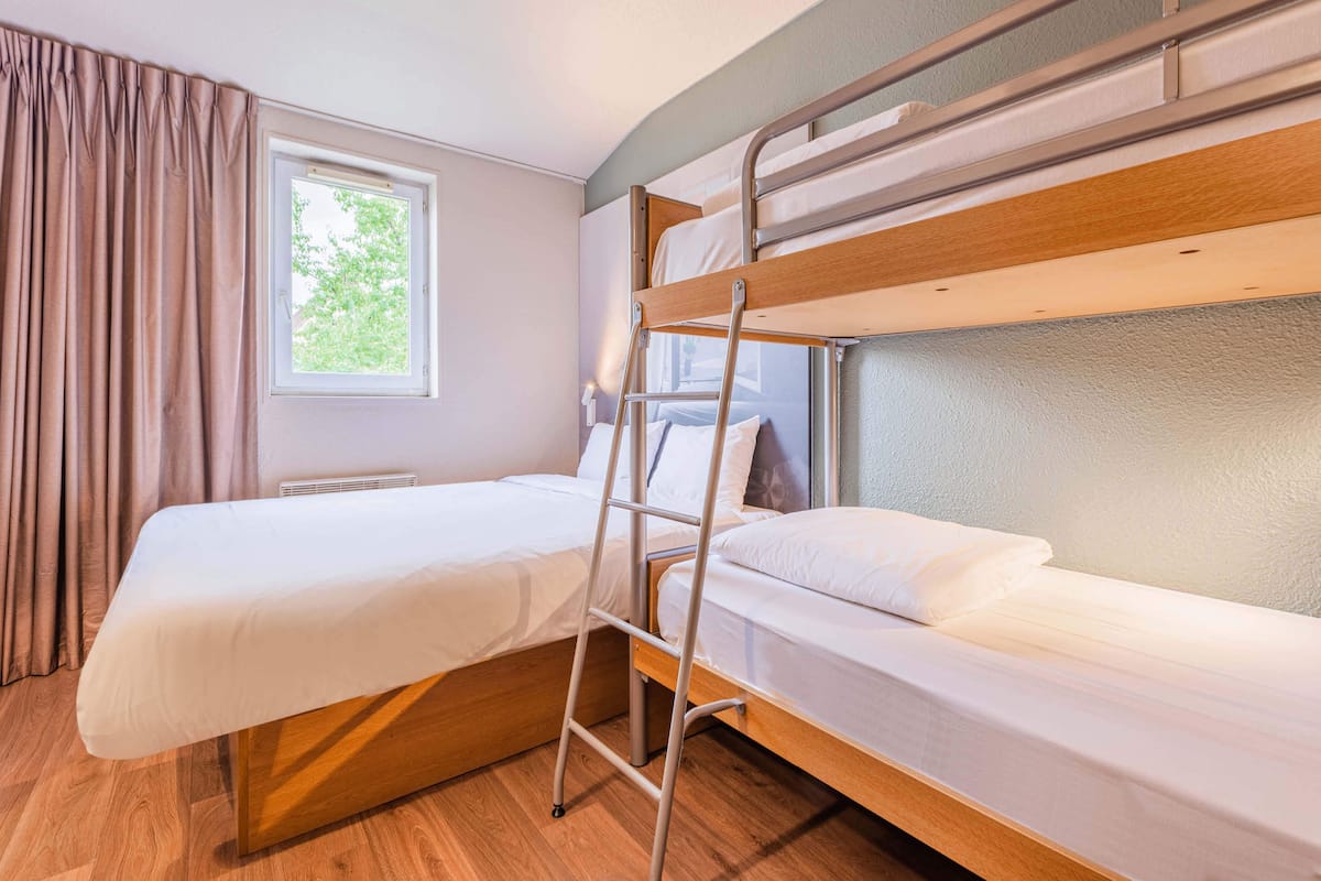 Een slaapkamer met een stapelbed, een raam met gordijnen en een radiator.