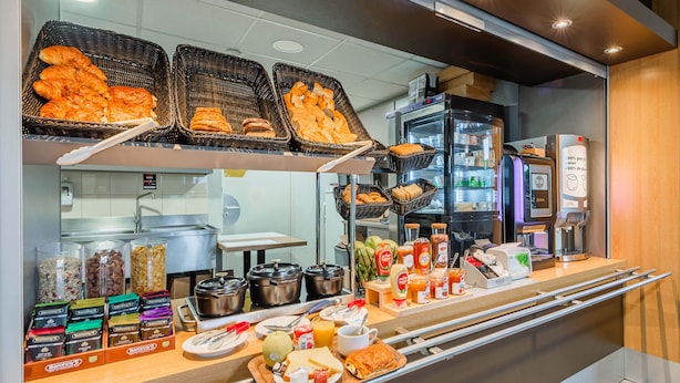 Een ontbijtbuffet met diverse gerechten, broodbaskets, toevoegingen en een koffieapparaat.
