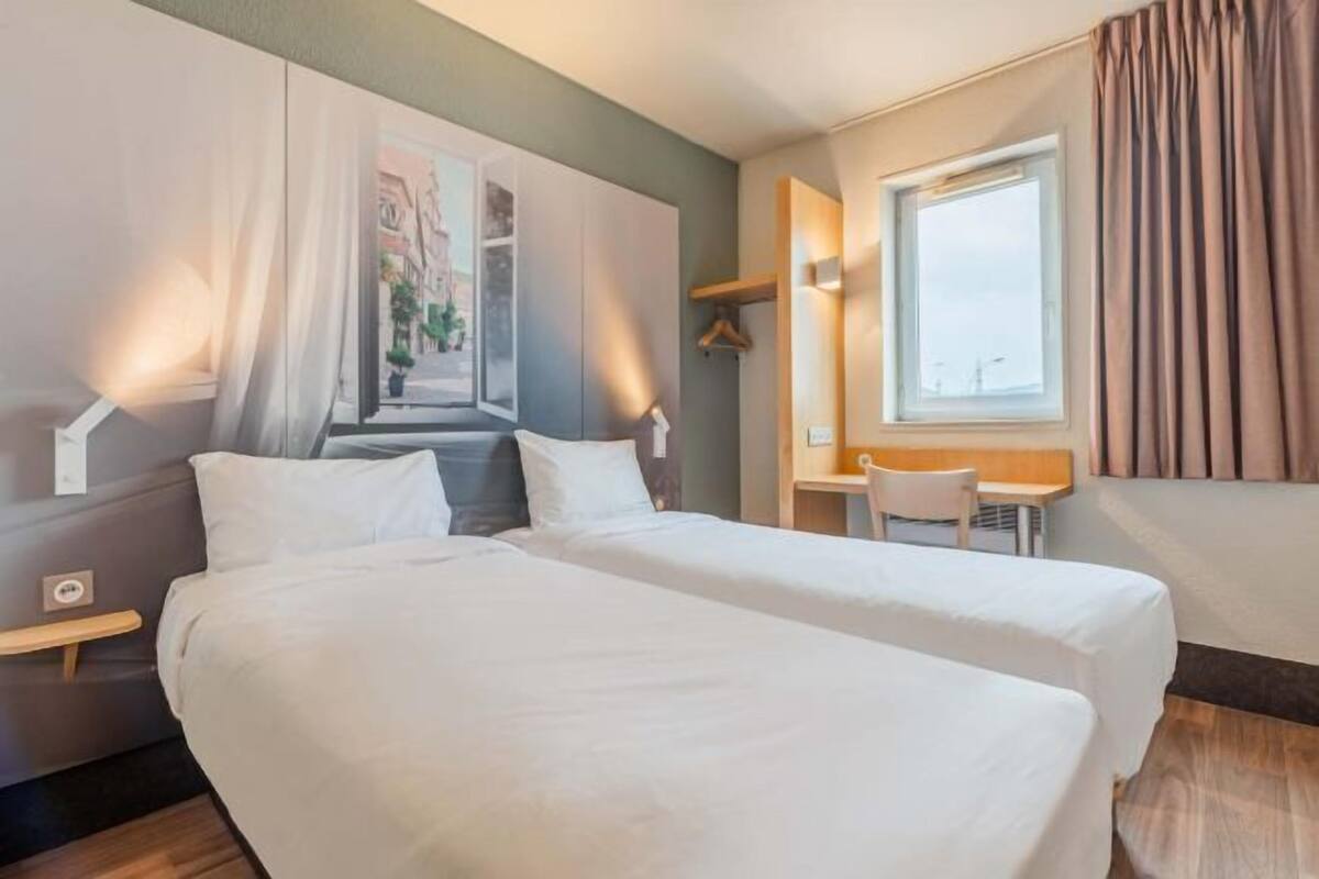 Een hotelkamer met twee bedden, een bureau, een stoel, een raam en een wandplank.