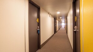 Een hotelgang met deuren aan beide kanten, een tapijtvloer en een gele wand.