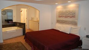 Un dormitorio con una cama grande, un baño con bañera y un pasillo que lleva a otra habitación.
