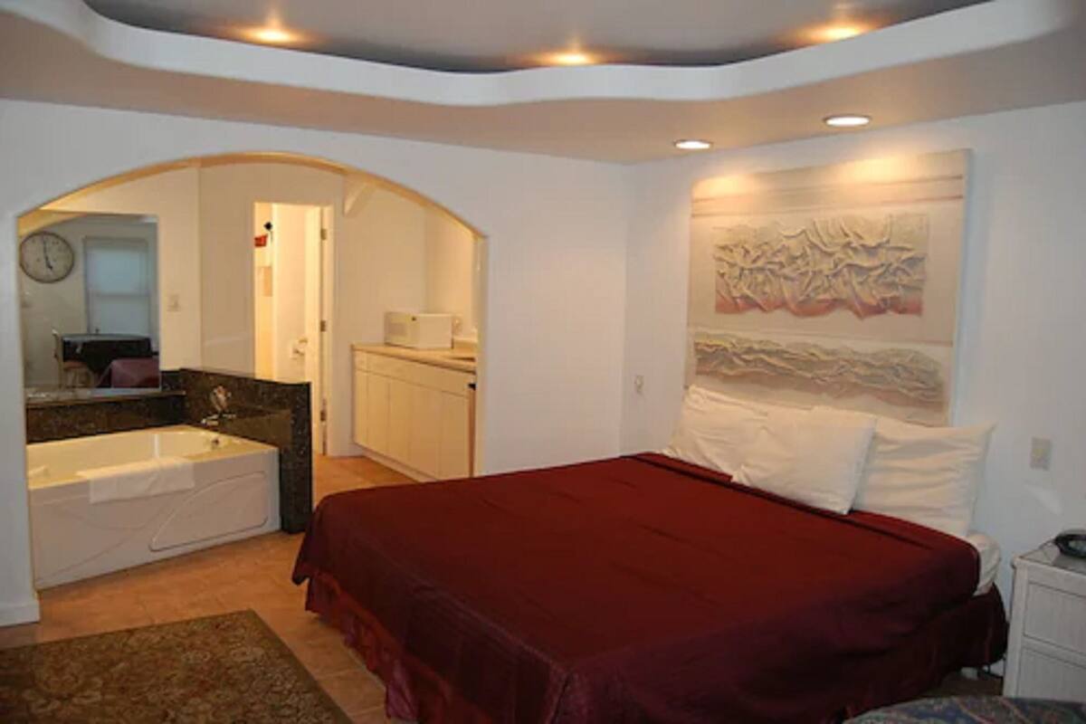 Un dormitorio con una cama grande, un baño con bañera y un pasillo que lleva a otra habitación.