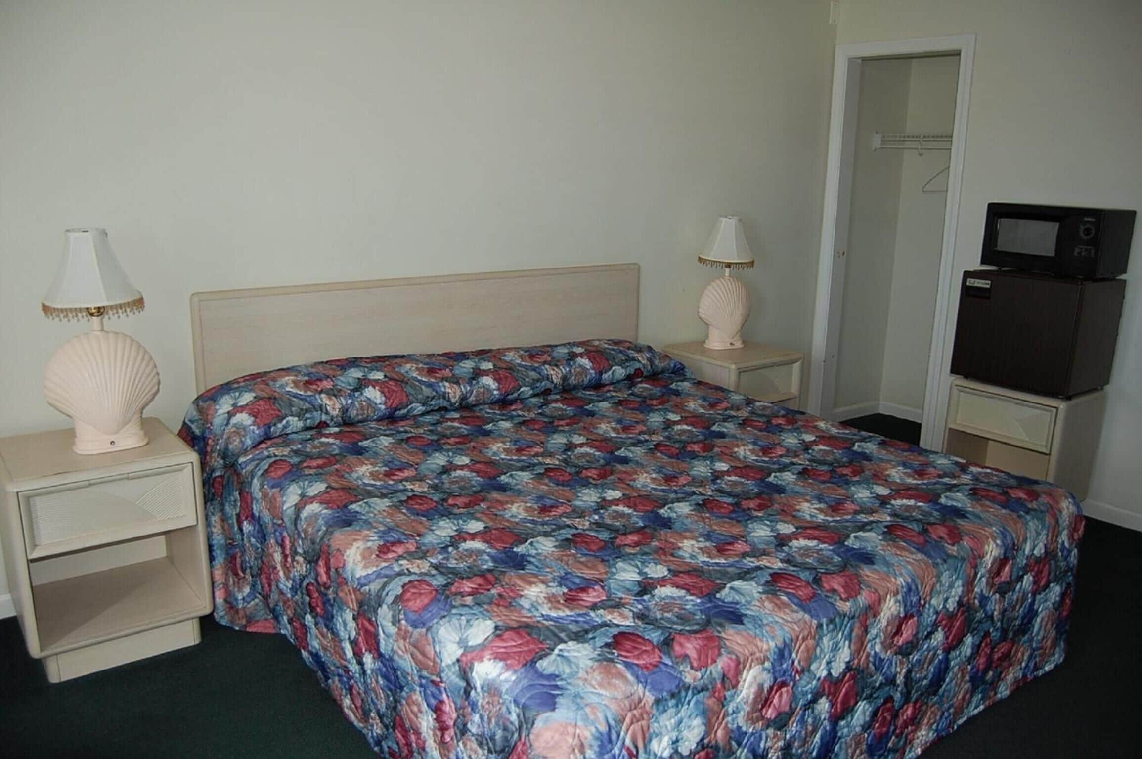 A bedroom with a floral bedspread, two bedside lamps, a television on a cabinet, and a wardrobe.