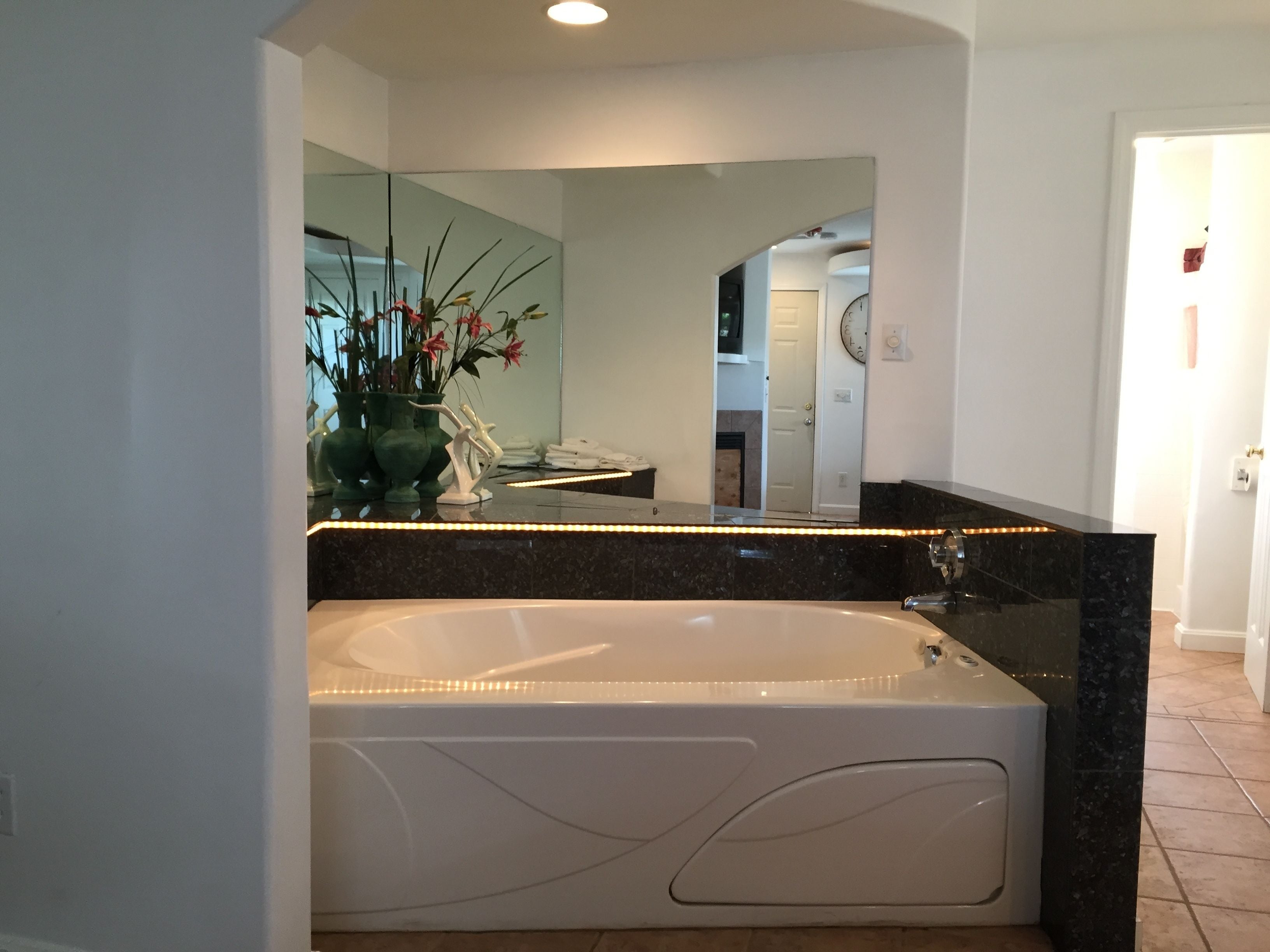 A modern bathroom with a freestanding bathtub, a large mirror, and a vase with flowers on the vanity.