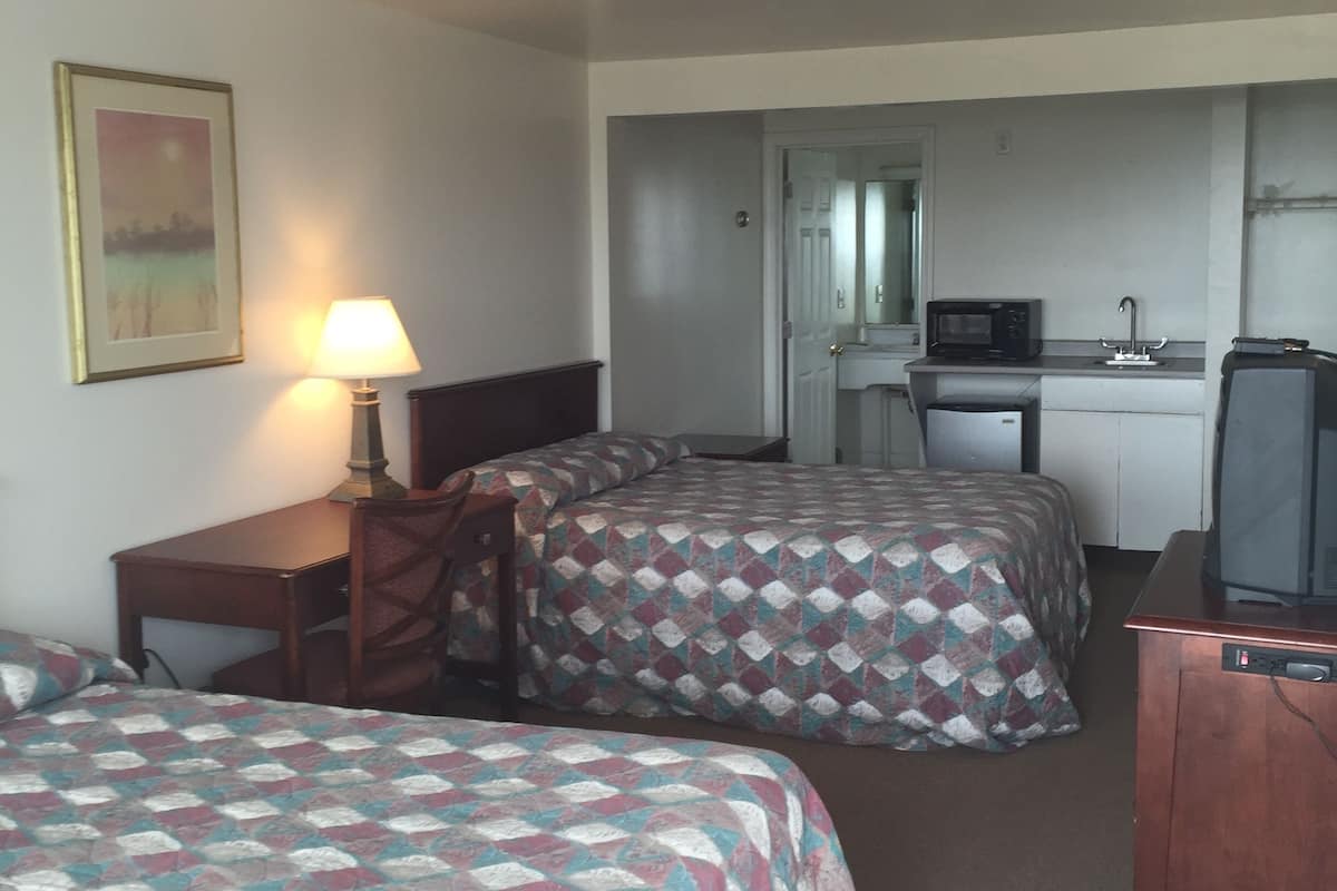 Habitación de hotel con dos camas, un escritorio, una silla, televisor, microondas y una pequeña cocina.