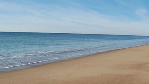 Una playa con cielo despejado y mar tranquilo.