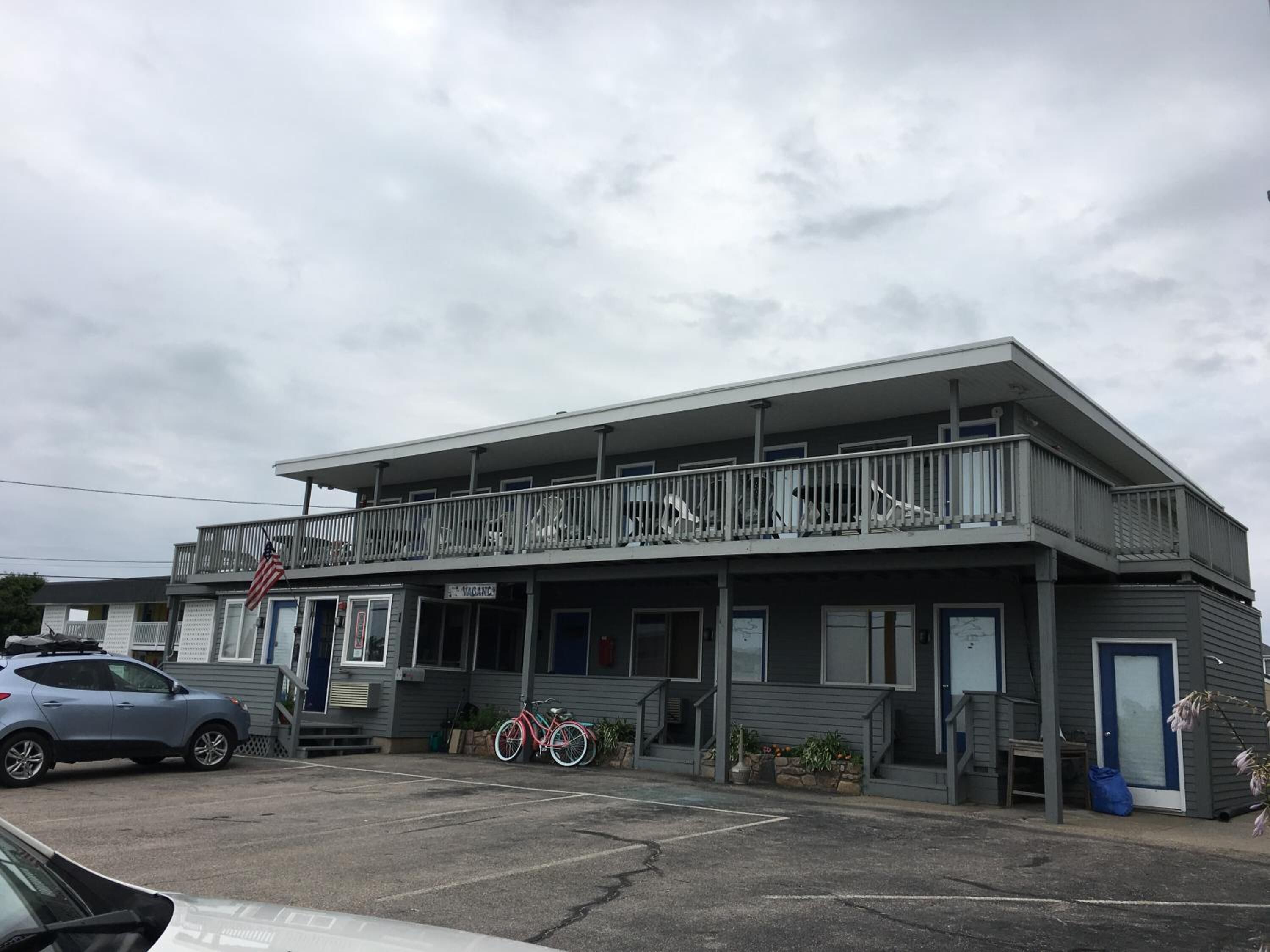 A motel with a balcony, a bicycle, and a car parked in front.