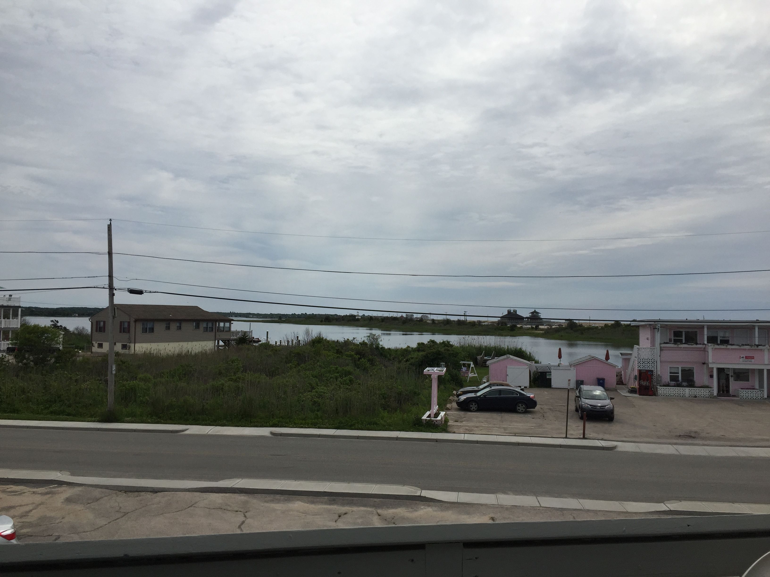 A parking lot with several cars, a building with a pink facade, and a body of water in the background.
