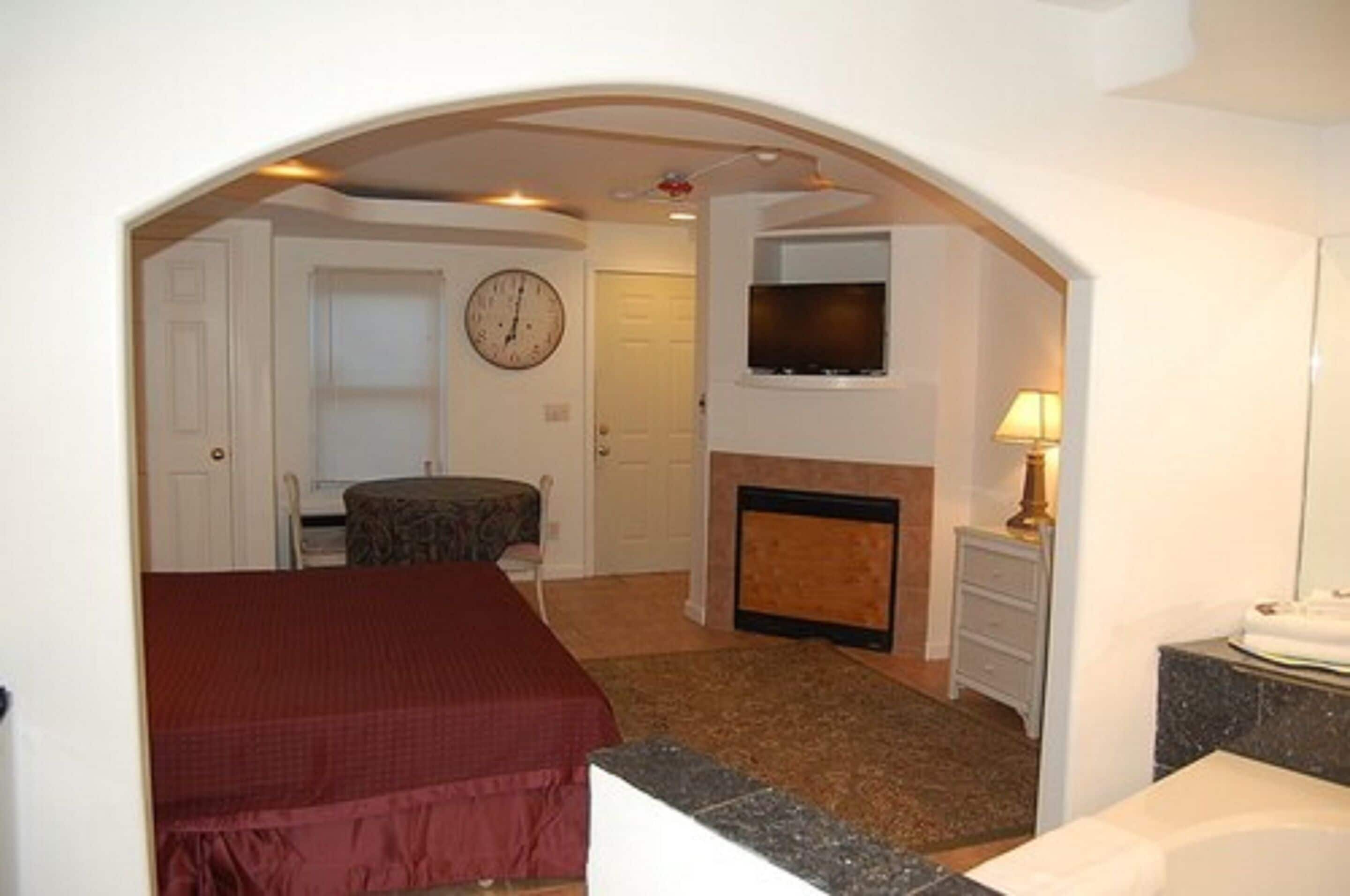 Une chambre à coucher comprenant un lit, une horloge, un téléviseur, une cheminée et une salle de bain avec un lavabo et un miroir.