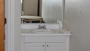 Un baño con lavamanos, espejo y armarios blancos.