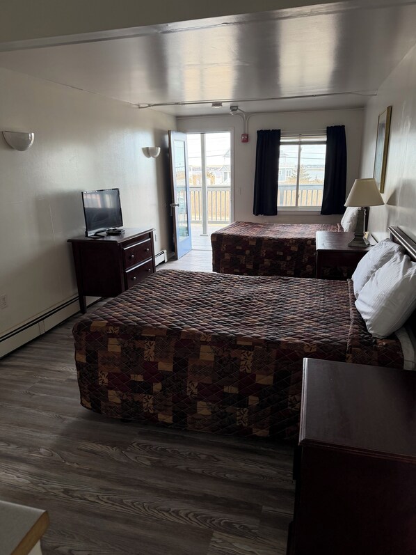 A hotel room with two beds, a television, a lamp, and a view of the outside.