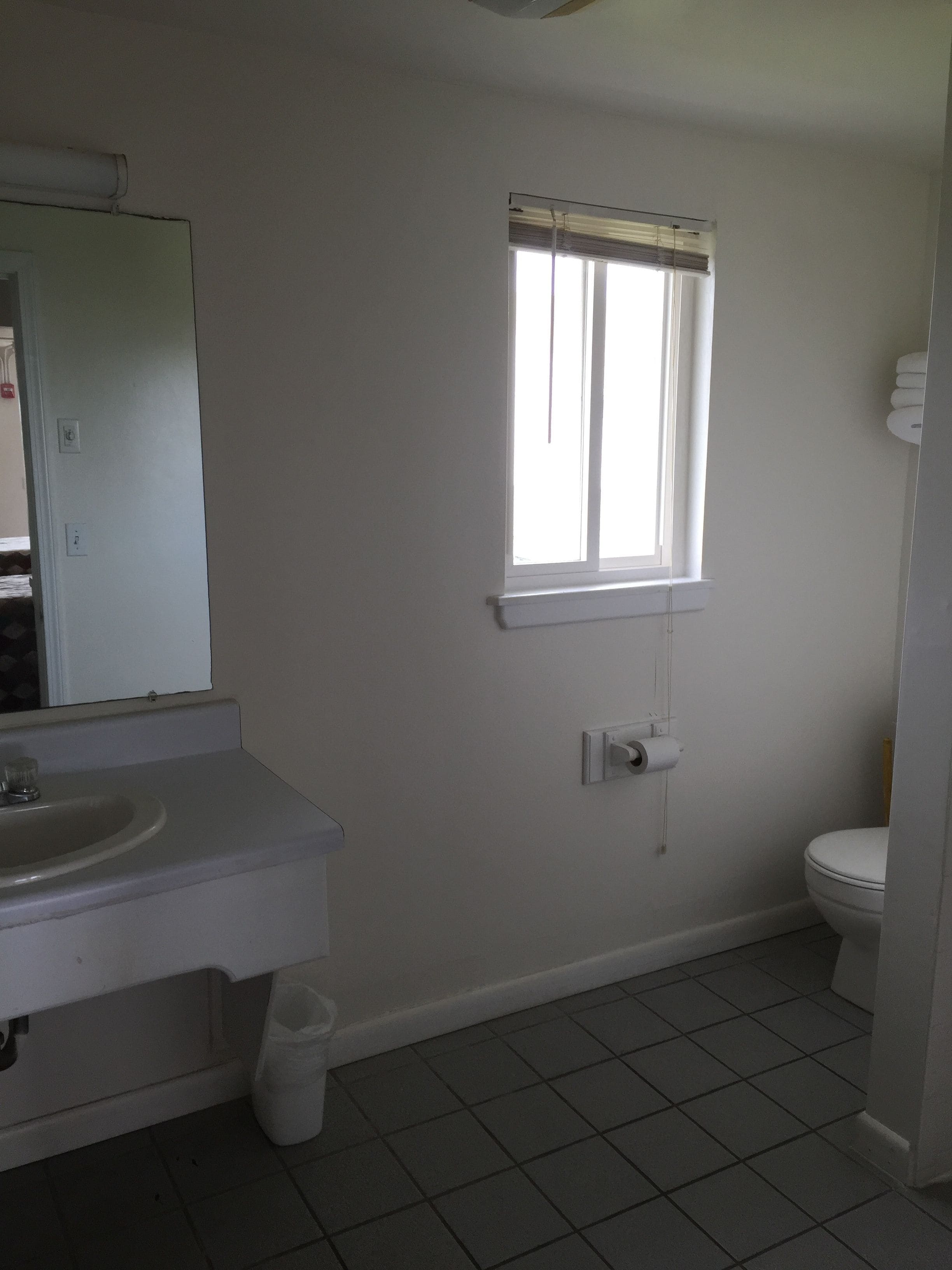 Un baño con lavamanos, inodoro y ventana con persianas.