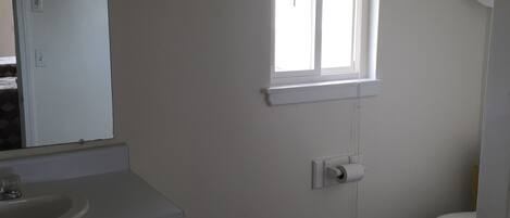 Un baño con lavamanos, inodoro y ventana con persianas.