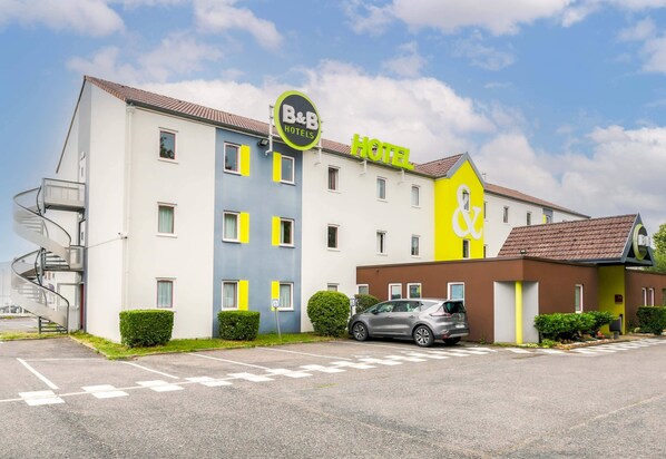 A B&B hotel with a modern design, featuring a parking lot and a car parked in front. - B&B HOTEL Nancy Laxou Zénith (Laxou)