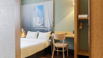Habitación de hotel con cama, escritorio con silla, un cuadro en la pared y una repisa con toallas.