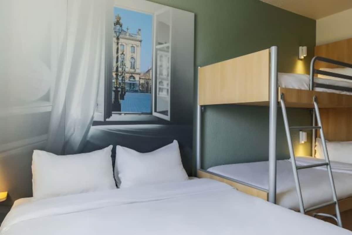 A hotel room with a bed, a bunk bed, and a large window with a view of a building.