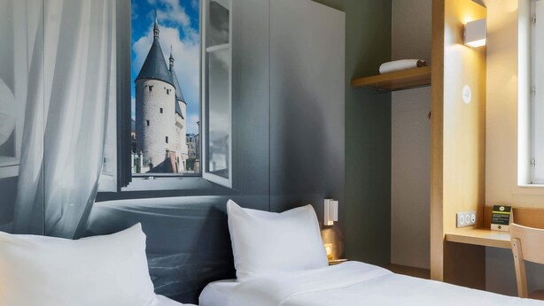 Habitación de hotel con dos camas, un ventanal con vistas a una torre, una mesita de noche con una lámpara y un escritorio pequeño con una silla.