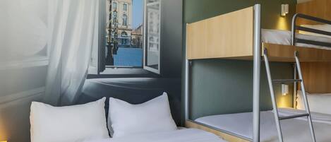 Habitación de hotel con literas, un ventanal con vistas a un edificio histórico y una cortina entreabierta al lado.
