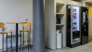 Un espacio de descanso con dos mesas y sillas de madera, una máquina expendedora y un bote de basura.