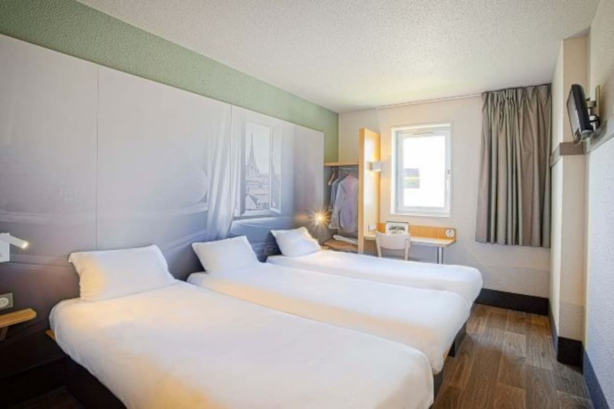 Habitación de hotel con dos camas, un escritorio, una silla, un armario y una ventana con cortinas.