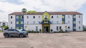 A B&B hotel with a modern design, featuring a parking lot and a parked car. - B&B HOTEL Mulhouse Ile Napoléon (Illzach)
