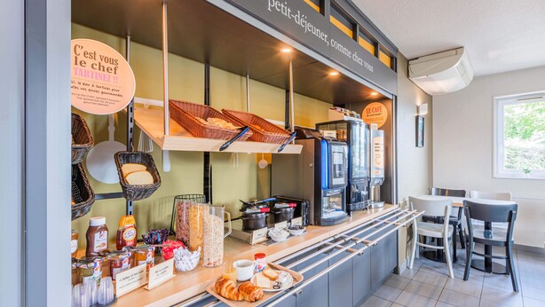A breakfast bar with baskets of bread, coffee machines, and various breakfast items. - B&B HOTEL Mulhouse Ile Napoléon (Illzach)