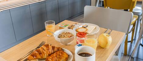 Una mesa de desayuno con croissants, cereales, yogur, jugo y un muffin.