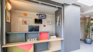 A reception desk with a computer, a flat-screen TV, and framed pictures on the wall. - B&B HOTEL Mulhouse Ile Napoléon (Illzach)