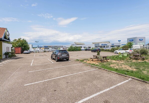 A parking lot with several cars, a picnic area, and a building with a Ford logo.