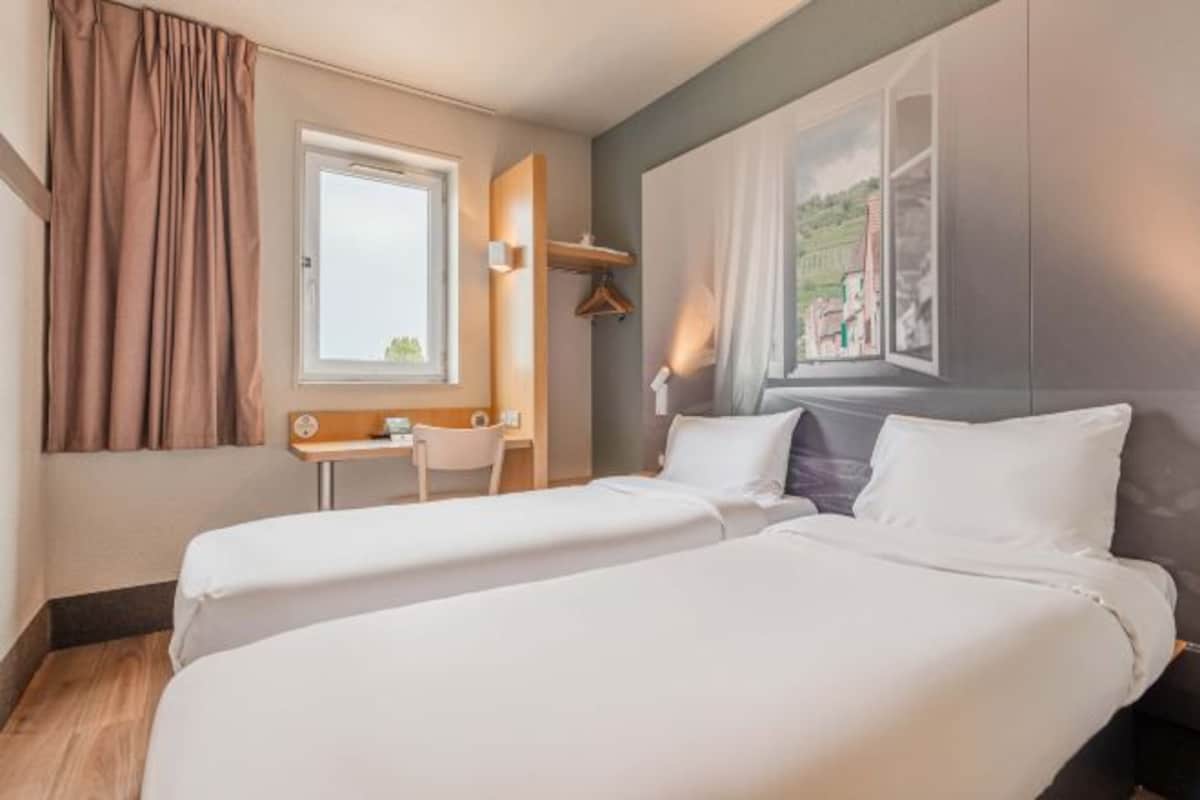 Habitación de hotel con dos camas, un escritorio, una silla y ventana con vistas al paisaje.