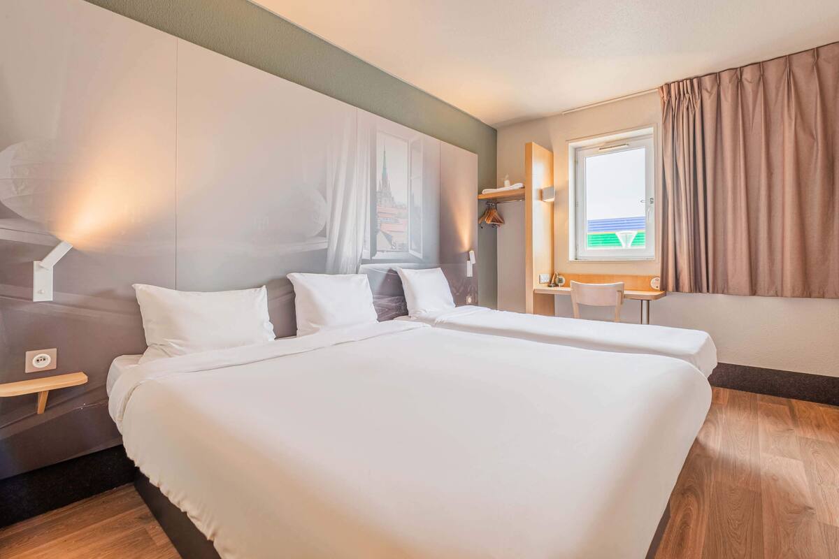 A hotel room with a large bed, a desk, a chair, and a window with curtains.