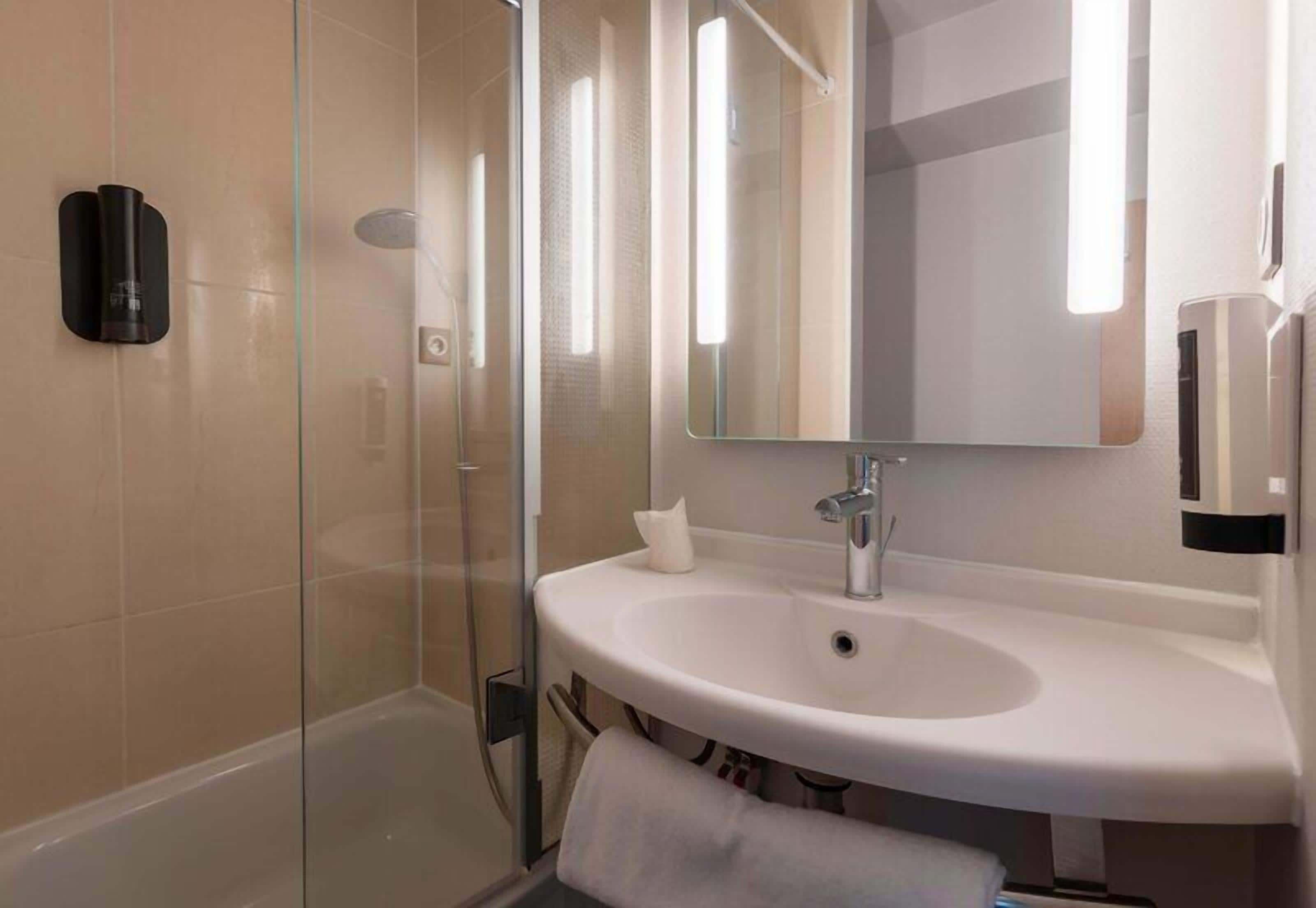 A bathroom with a glass shower enclosure, a white sink, a mirror, and a towel rack.