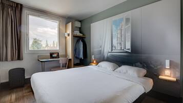 Een moderne hotelkamer met een groot bed, een bureau met stoel, een kledingkast en een groot raam met gordijnen.