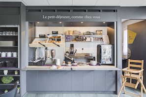 Un café con un mostrador que exhibe pasteles y café, una zona de estar con una silla, y estanterías con utensilios de cocina.