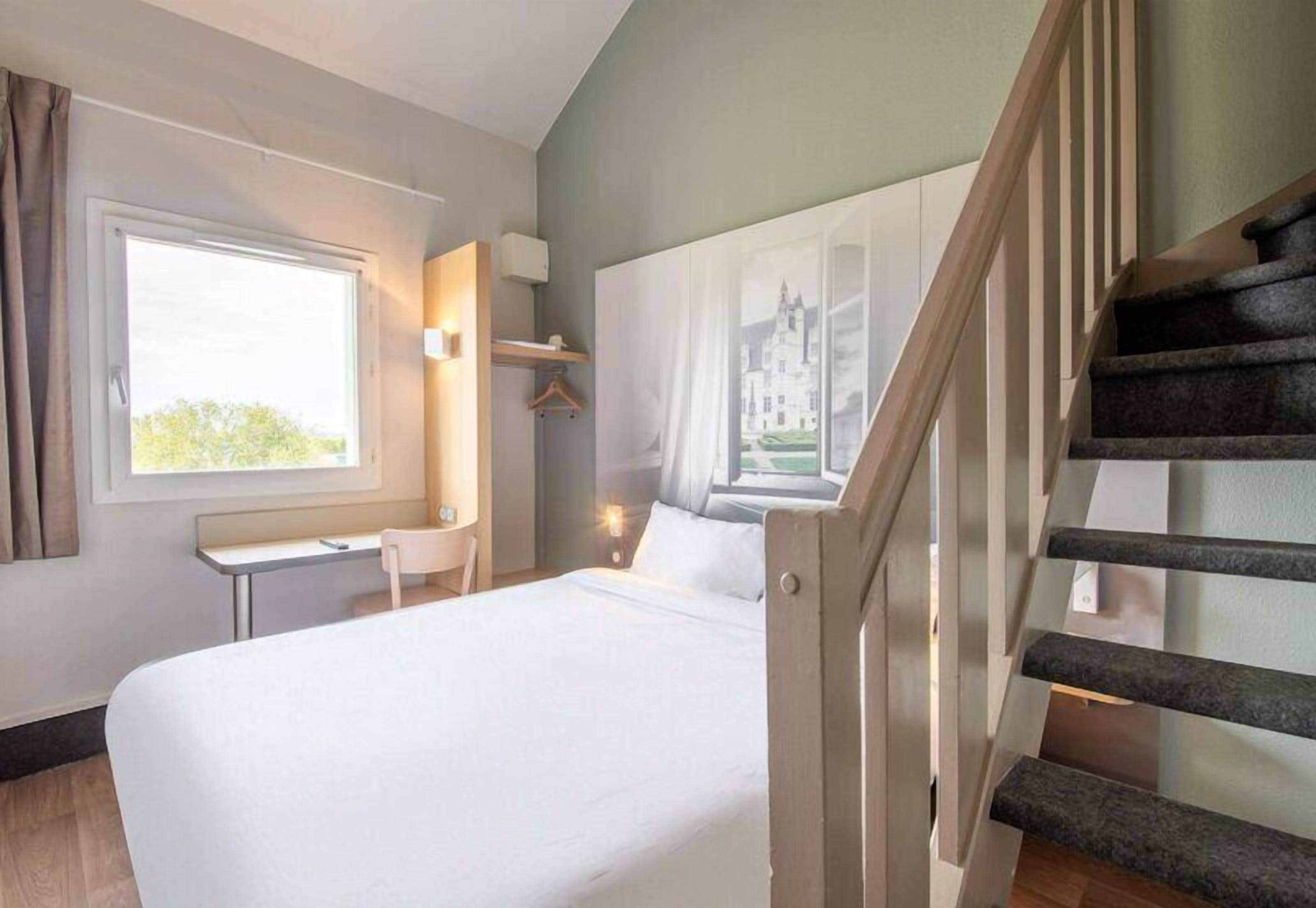 Et hotelværelse med seng, skrivebord, stol, et vindue og en trappe.