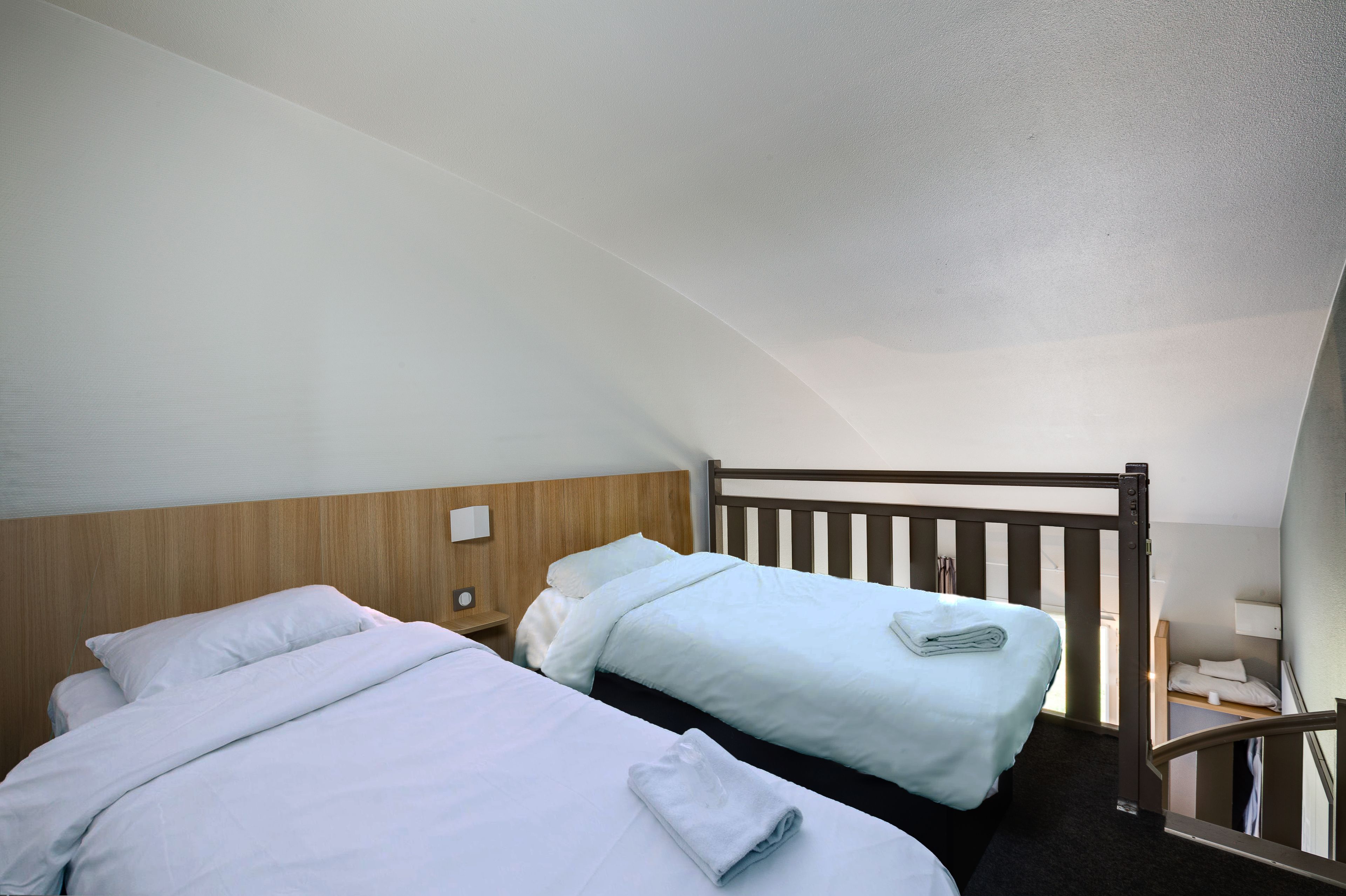 Habitación de hotel con dos camas, cabeceros de madera y una mesita de noche pequeña con lámpara.