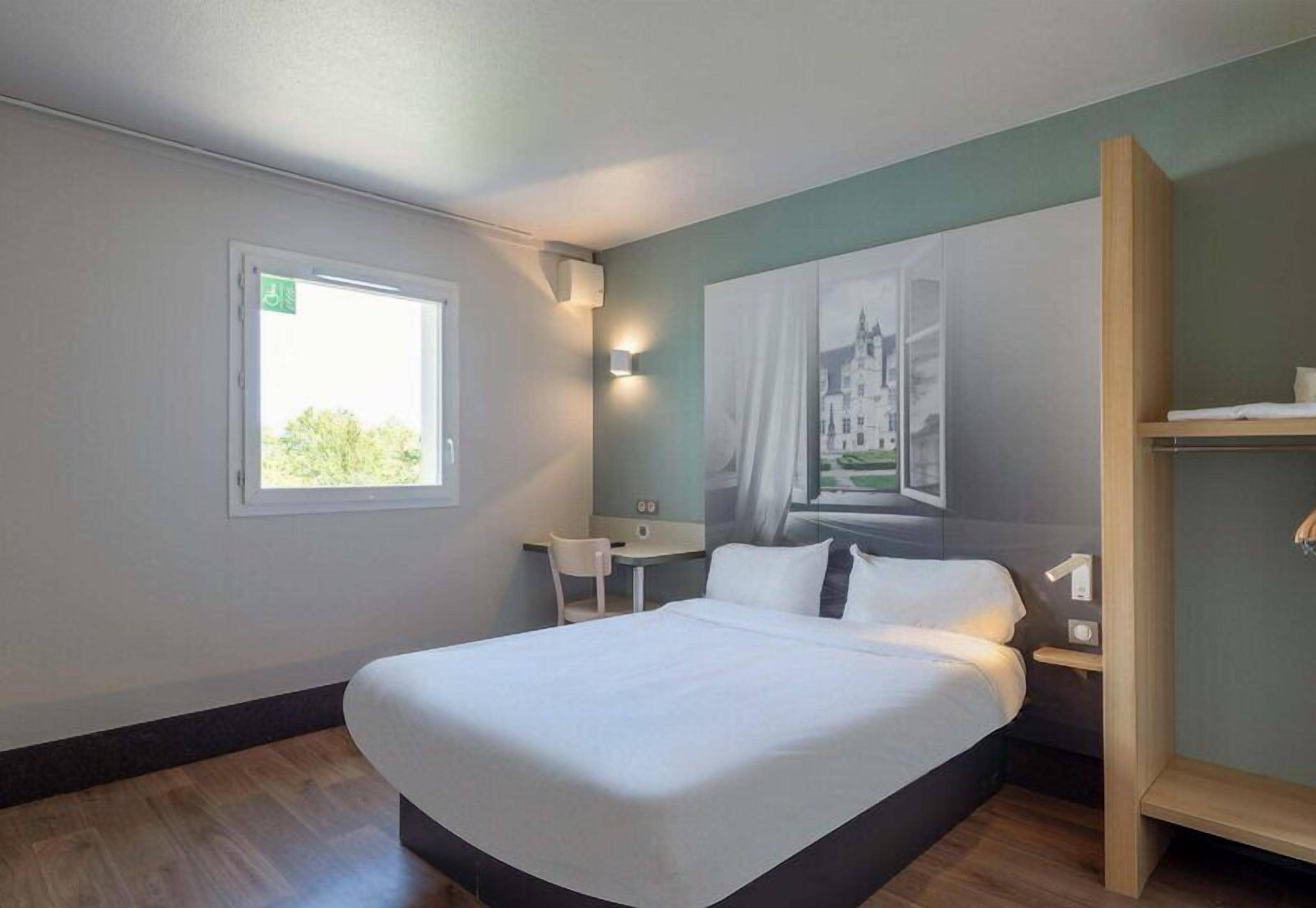 A hotel room with a bed, a desk, a chair, and a window.