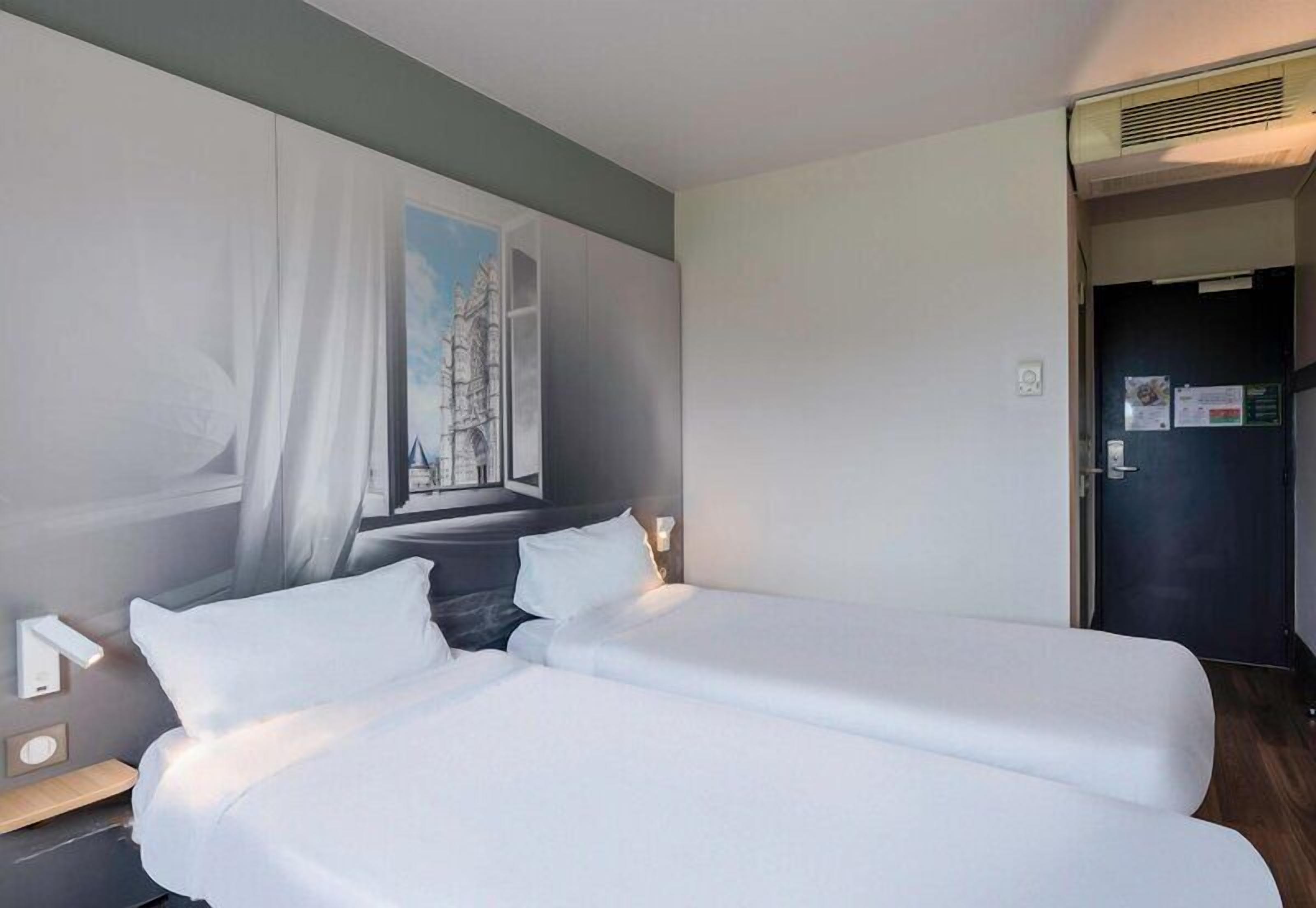 A hotel room with two beds, a painting on the wall, a window with curtains, and a door with a sign.