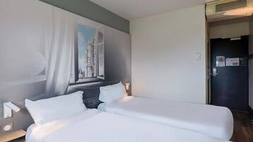 A hotel room with two beds, a painting on the wall, a window with curtains, and a door with a sign.