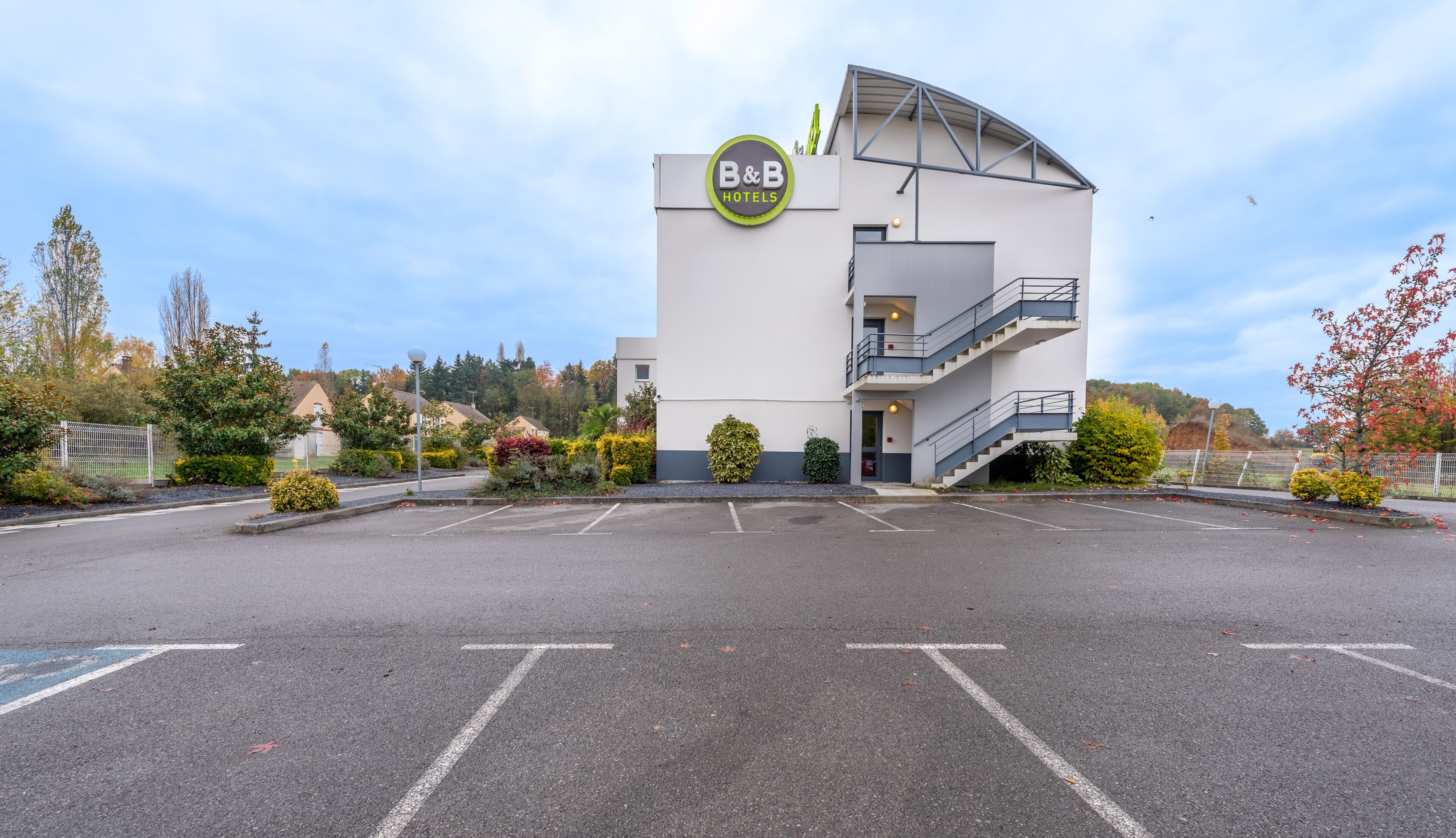A B&B hotel with a modern design, featuring a parking lot and landscaped garden.