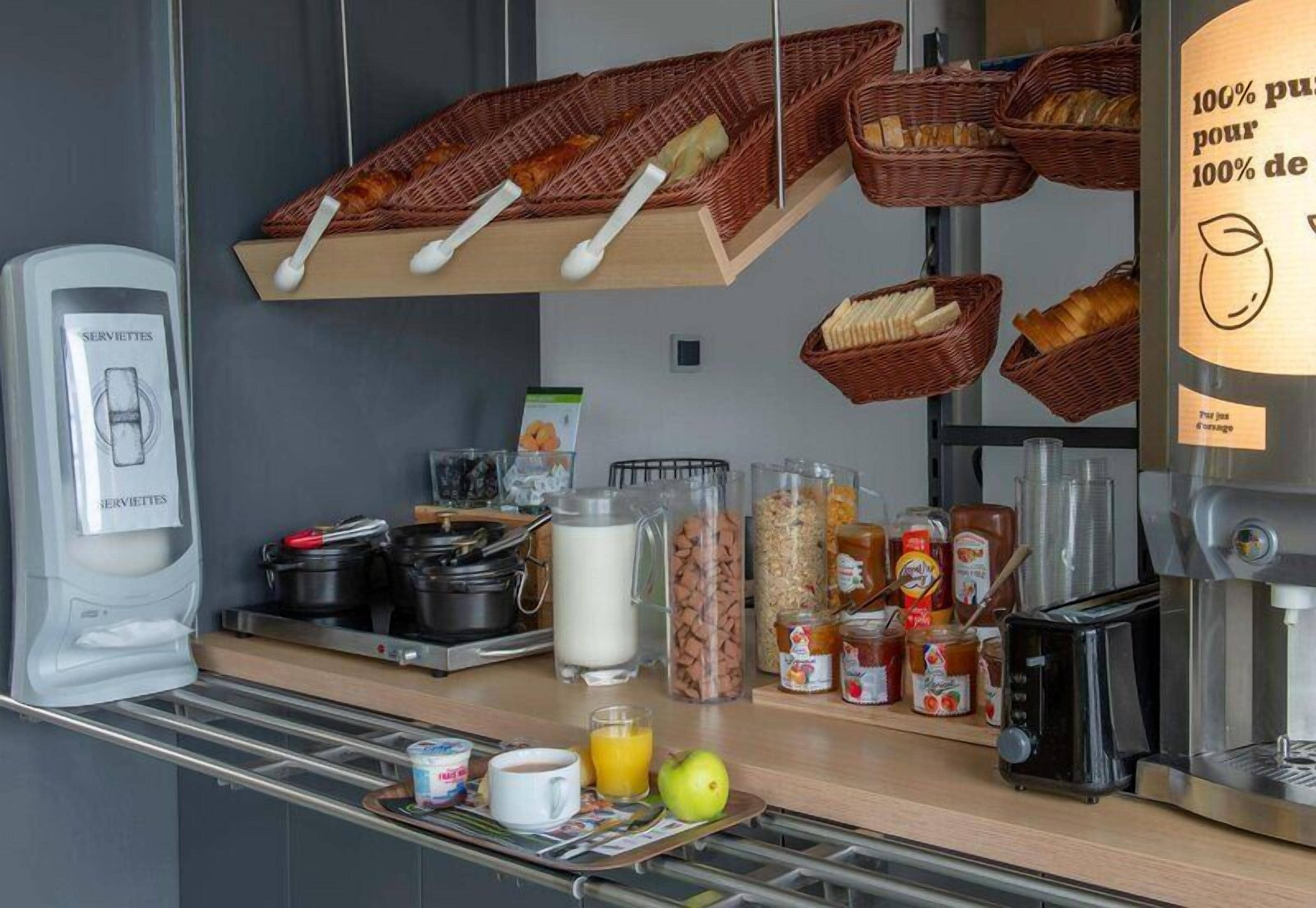 Un bar à petit-déjeuner avec des paniers de pain, des pots de confitures, une machine à café et un distributeur de lait.