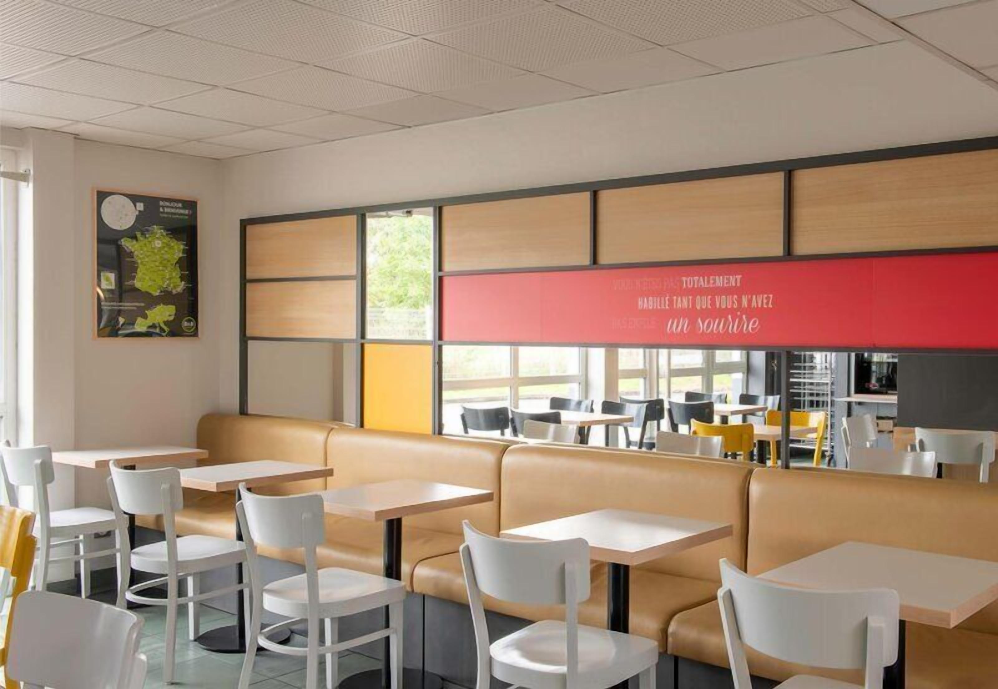 Un área de comedor moderna con cabinas y mesas, una pared de acento roja y un cartel en la pared.
