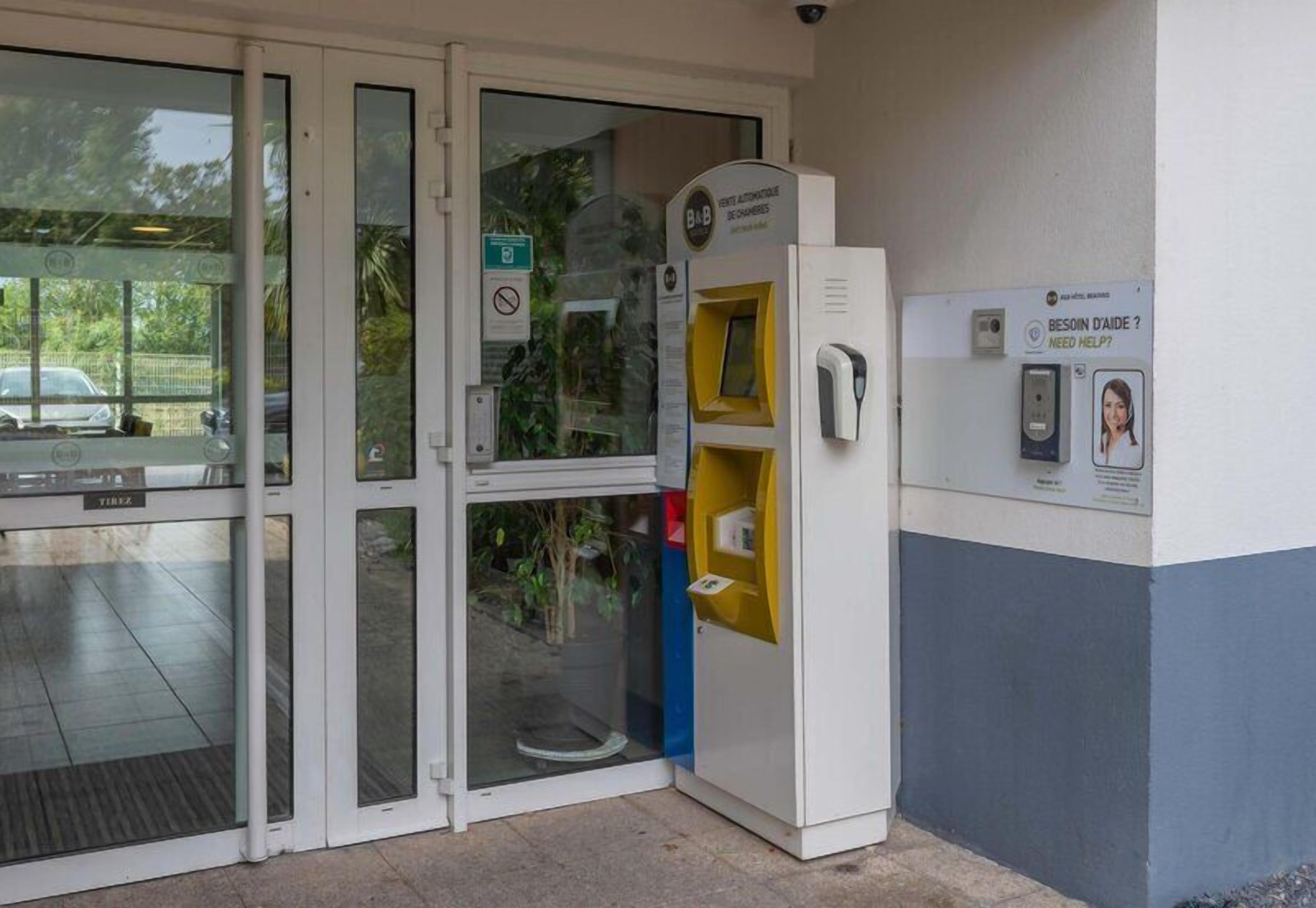 A building entrance with a glass door, a yellow vending machine, and a sign indicating a need for help.