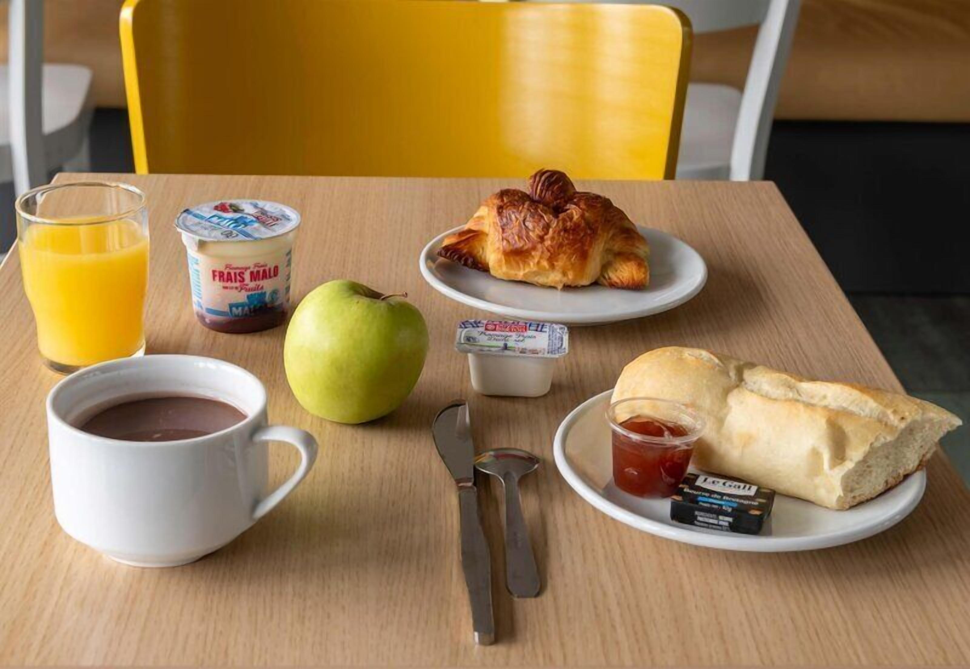 A breakfast table with a croissant, apple, juice, yogurt, and bread.