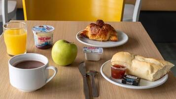 A breakfast table with a croissant, apple, juice, yogurt, and bread.